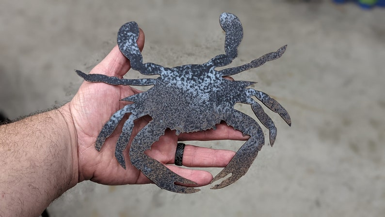 May include: A metal crab sculpture with a rustic, weathered finish. The crab is in a raised position with its claws extended.