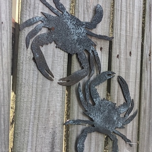 May include: Two metal crab silhouettes attached to a wooden fence. The crabs are painted a dark gray with a weathered finish.
