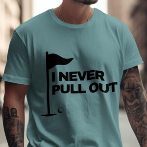 May include: A light blue t-shirt with a black golf flag and golf ball graphic. The text "I NEVER PULL OUT" is printed in black on the shirt.