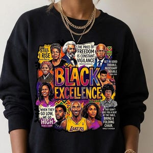 May include: Black sweatshirt featuring a colorful graphic with the words "BLACK EXCELLENCE" and portraits of notable figures. The design includes quotes and the Lakers logo. The sweatshirt is worn by a person.