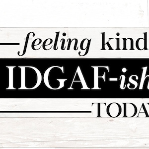 Op de afbeelding: Een zwart-wit bord met de tekst "feeling kinda IDGAF-ish TODAY" op een witte houten achtergrond.