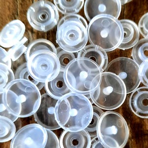 Peut inclure: Gros plan sur un tas de boutons-pression en plastique transparent. Les boutons-pression sont ronds et ont un petit centre surélevé.