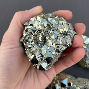 May include: A large, irregularly shaped cluster of pyrite crystals. The crystals are a metallic gold color and have a sharp, faceted appearance. The cluster is about the size of a person's hand.