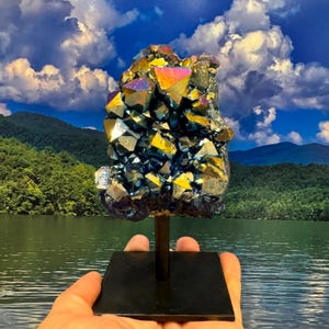 May include: A large, iridescent blue and gold crystal cluster on a black metal stand. The crystal is a cluster of many smaller crystals, and it has a rough, natural texture.