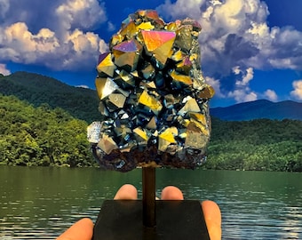 May include: A large, iridescent blue and gold crystal cluster on a black metal stand. The crystal is a cluster of many smaller crystals, and it has a rough, natural texture.