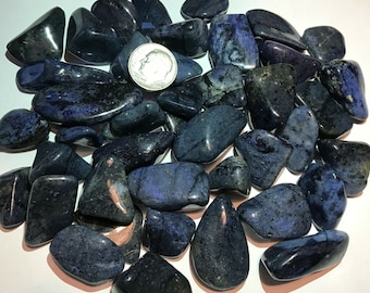 May include: A collection of tumbled blue and black denim lapis lazuli stones. The stones are smooth and polished, with a variety of shapes and sizes.