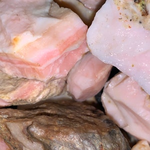 May include: A close-up of a pile of pink and white opal stones. The stones are rough and have a natural, unpolished look.