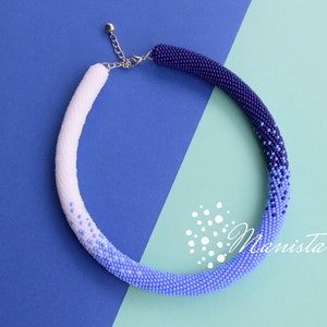 Könnte beinhalten: Eine weiße, blaue und violette Perlenkette mit einem silbernen Verschluss. Die Kette ist im Ombre-Stil gehalten, wobei die weißen Perlen oben und die violetten Perlen unten sind.