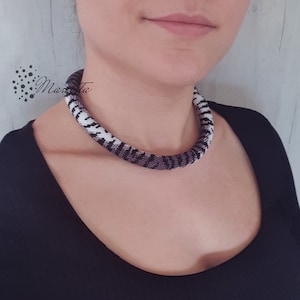 May include: A close-up of a woman wearing a black choker necklace with a white and purple geometric pattern. The necklace is made of small beads and is very detailed.
