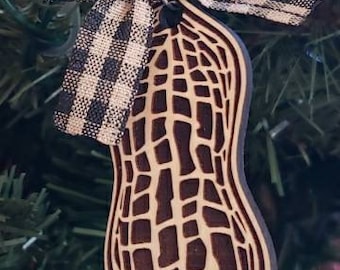 May include: A wooden peanut-shaped ornament with a brown and white checkered bow. The ornament is decorated with a detailed peanut shell design.