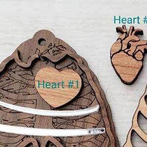 May include: Two wooden heart ornaments, one with a detailed anatomical design and the text "Heart #2", and the other with a simple heart shape and the text "Heart #1".