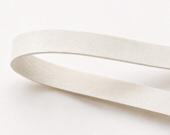 May include: A single, continuous strip of off-white, textured paper material folded into a simple loop. The surface of the paper shows a subtle, fibrous grain and a matte finish, with the strip curving gracefully to create an open, rounded shape.
