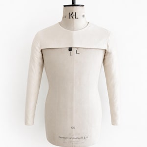 May include: A beige fabric dress form with long sleeves and a round neckline. The torso features the text KL, GK, and Kennett & Lindsell Ltd printed in black. The mannequin is mounted on a black stand and has a structured, professional appearance.