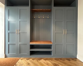 May include: A gray painted entryway with three sets of double doors, a wooden shelf with hooks, and a wooden bench. The floor is a herringbone pattern of light brown wood.