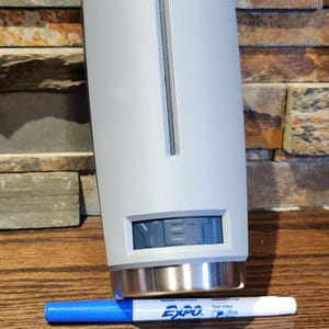 May include: A gray Yeti tumbler with a stainless steel lid and the word "YETI" printed on the side. The tumbler is sitting on a wooden surface.