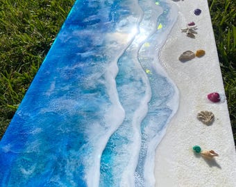 May include: A blue and white resin art piece depicting ocean waves crashing on a white sandy beach. The piece is decorated with small seashells.