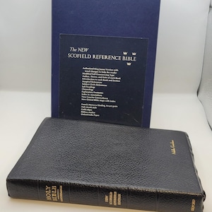 Könnte beinhalten: Eine schwarze, ledergebundene Heilige Bibel mit goldener Schrift und einem passenden blauen Etui. Der Text auf dem Etui lautet "The New Scofield Reference Bible". Es ist eine Oxford-Ausgabe.