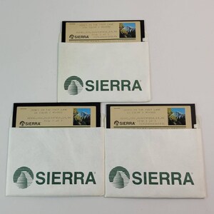 Può includere: Tre floppy disk vintage in buste di carta bianca. I dischi sono etichettati "JONES IN THE FAST LANE" con un'immagine di montagna. Le buste hanno il logo "SIERRA" stampato in verde.