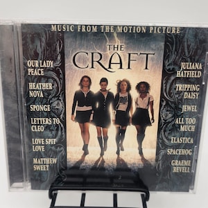 May include: A CD case for the motion picture soundtrack The Craft. The cover features four individuals in dark clothing walking forward against a rainy background. The text lists artists including Our Lady Peace, Heather Nova, and Jewel.