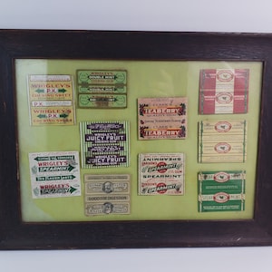 May include: Framed collection of vintage chewing gum wrappers, including Wrigley's Double Mint, Juicy Fruit, and Spearmint. The wrappers are in various colors, including green, red, and white, and are arranged on a light green background within a dark brown wooden frame.