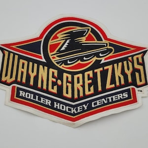 May include: Embroidered patch with the text "WAYNE-GRETZKY'S ROLLER HOCKEY CENTERS" in gold. The patch has a red, black, and white colour scheme with a stylized roller skate graphic. The patch is in a shield shape.