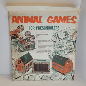 Op de afbeelding: Een vintage doos spel voor kleuters genaamd "Animal Games". De doos heeft een kleurrijke illustratie van kinderen die spelen met dierenkaarten en drie houten huizen. Het spel bevat 24 moeder- en babydierenkaarten, een huis, een dierentuin, een schuur en een boerderij.