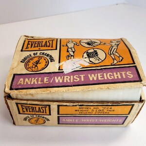 May include: A vintage box of Everlast ankle and wrist weights. The box is orange and purple with the Everlast logo and the words "Choice of Champions". The box is labeled "Ankle/Wrist Weights" and has a model number of 7014. The weights are 5 pounds per pair and have Velcro zippers.