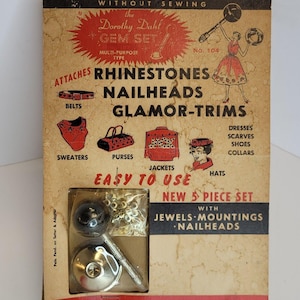 May include: A vintage package for a "Do It Yourself" rhinestone and nailhead trim kit. The package features a red, white, and blue color scheme and includes a tool for attaching the rhinestones and nailheads. The package also includes a variety of uses for the trim, including belts, sweaters, purses, jackets, and hats. The text on the package reads "The Dorothy Dahl Gem Set, Multi-Purpose Type, No. 104, Attaches Rhinestones, Nailheads, Glamor-Trims, Easy to Use, New 5 Piece Set with Jewels, Mountings, Nailheads, Glamorize Your Wardrobe."