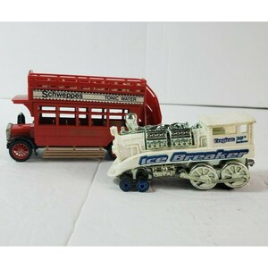 May include: Two toy vehicles: a red double-decker bus with "Schweppes TONIC WATER" text and a white "Ice Breaker" train with "Engine 32° below" text. The bus has black wheels, and the train has silver wheels and blue accents.