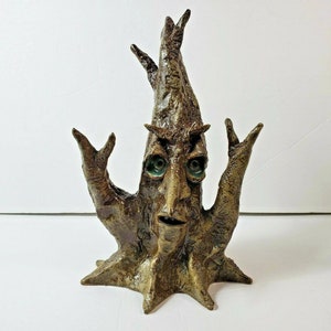 May include: A whimsical, handcrafted ceramic tree sculpture with a face and arms raised in a gesture. The tree has a textured, brown finish with green eyes. The sculpture is a unique decorative item.