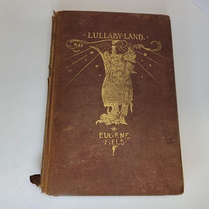 May include: A brown book with gold lettering on the cover. The title is "Lullaby-Land" by Eugene Field. The cover features an illustration of an angel holding a candle.