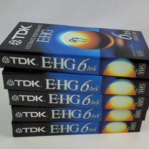 May include: A stack of six TDK EHG VHS video tapes, each with a blue and yellow design and the text "TDK EHG 6 hrs" printed on the front.