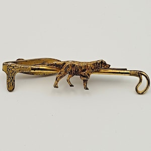 May include: A gold-toned tie tack featuring a detailed sculpted image of a dog walking with a walking stick.