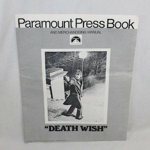 May include: A Paramount Press Book and Merchandising Manual featuring a black and white image from the film "Death Wish." The cover shows a man aiming a gun in a night street scene. The Paramount logo is present.