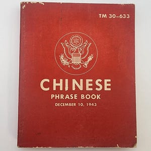 Op de afbeelding: Een vintage rood "Chinese Phrase Book" van 10 december 1943, met de tekst "TM 30-633" bovenaan. De omslag heeft een wit embleem en de titel in grote witte letters.