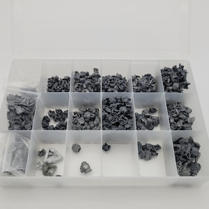 May include: A clear plastic organiser filled with small, grey, plastic components. The components are of various shapes and sizes, and are stored in individual compartments. The organiser is open, revealing the contents.