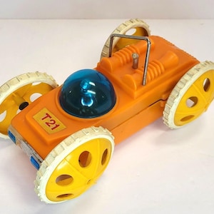 May include: Orange and yellow toy car with a blue dome on top. The car has a white rim around each wheel and the words "T21" on the side.