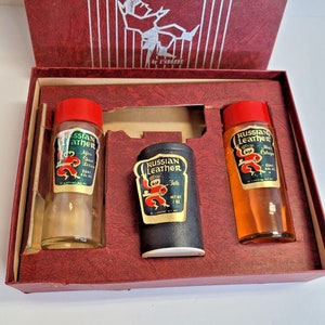 May include: A vintage "Russian Leather" grooming set in a red box. The set includes after shave lotion, talc, and cologne, each with a label featuring a dancing figure. The bottles have red caps and are in a red box.