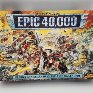 Peut inclure: Boîte de jeu Warhammer Epic 40,000 avec une illustration colorée d'une scène de bataille. La boîte présente le titre du jeu et le texte "Massive Armies Clash in the 41st Millennium". L'illustration représente divers véhicules et figurines dans un cadre de guerre.