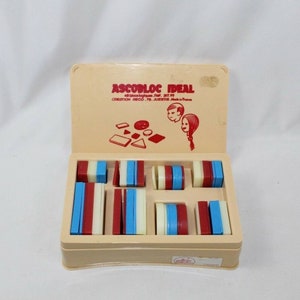 May include: A vintage Ascobloc Ideal toy set in a beige box. The set includes various geometric blocks in red, blue, and white. The box lid features the text "Ascobloc Ideal" and illustrations. A classic educational toy.