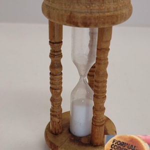 May include: A wooden hourglass with a clear glass bulb and white sand. The hourglass is labeled "FIORILAL WITH CODEINE CAPSULES (!!!)" on the bottom.
