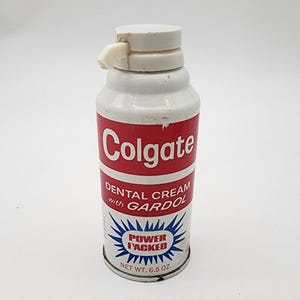 Könnte beinhalten: Eine weiße und rote Metalldose mit Colgate Zahncreme mit Gardol. Das Etikett zeigt den Schriftzug Colgate, Dental Cream with Gardol und Power Packed in einem blauen Stern. Das Nettogewicht ist mit 6,5 oz angegeben.