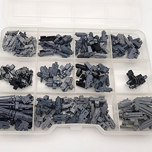 Puede incluir: Un organizador de plástico transparente lleno de varios modelos de pistolas en miniatura de plástico gris. Los compartimentos contienen diferentes tipos de armas de juguete, incluyendo ametralladoras y otras réplicas de armas de fuego.