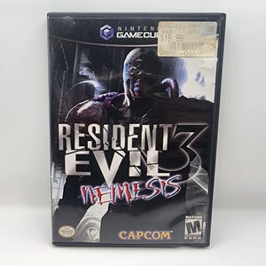May include: A Nintendo GameCube game case for Resident Evil 3: Nemesis. The cover shows a menacing creature with the game title in large, bold letters. The case is black with a sticker on the top right corner.