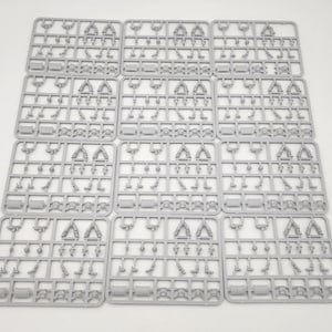 Puede incluir: Doce matrices de modelismo de plástico gris idénticas dispuestas en una cuadrícula. Cada marco rectangular contiene varios componentes en miniatura sin pintar, incluyendo extremidades pequeñas, piezas de torso y partes cilíndricas.