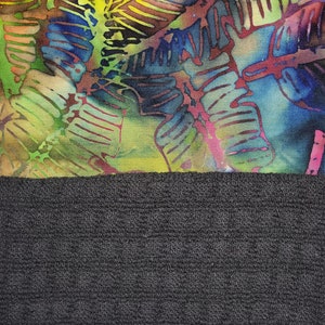 May include: A colourful fabric with a batik design of leaves in shades of blue, green, yellow, and red. The fabric is sewn to a black, textured fabric.
