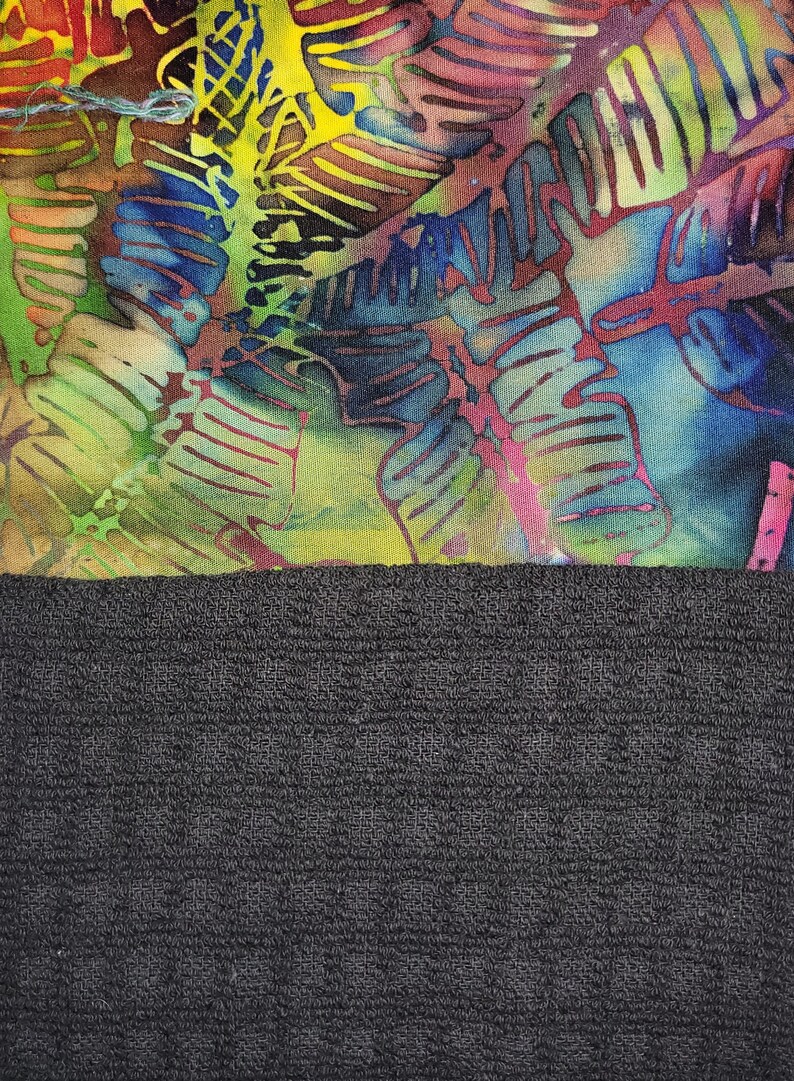 May include: A colourful fabric with a batik design of leaves in shades of blue, green, yellow, and red. The fabric is sewn to a black, textured fabric.