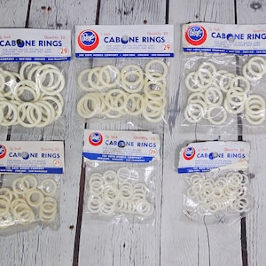 May include: Six packages of white plastic rings labeled "Boye Cabone Rings" in various sizes, including 1/2 inch, 5/8 inch, 3/4 inch, 1 inch, and 1 1/8 inch. The packages are labeled with the quantity of rings included, ranging from 20 to 36.