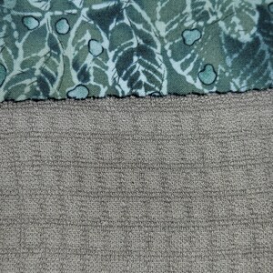 May include: A close-up of two different fabrics. The top fabric is a green and white patterned fabric. The bottom fabric is a grey textured fabric.