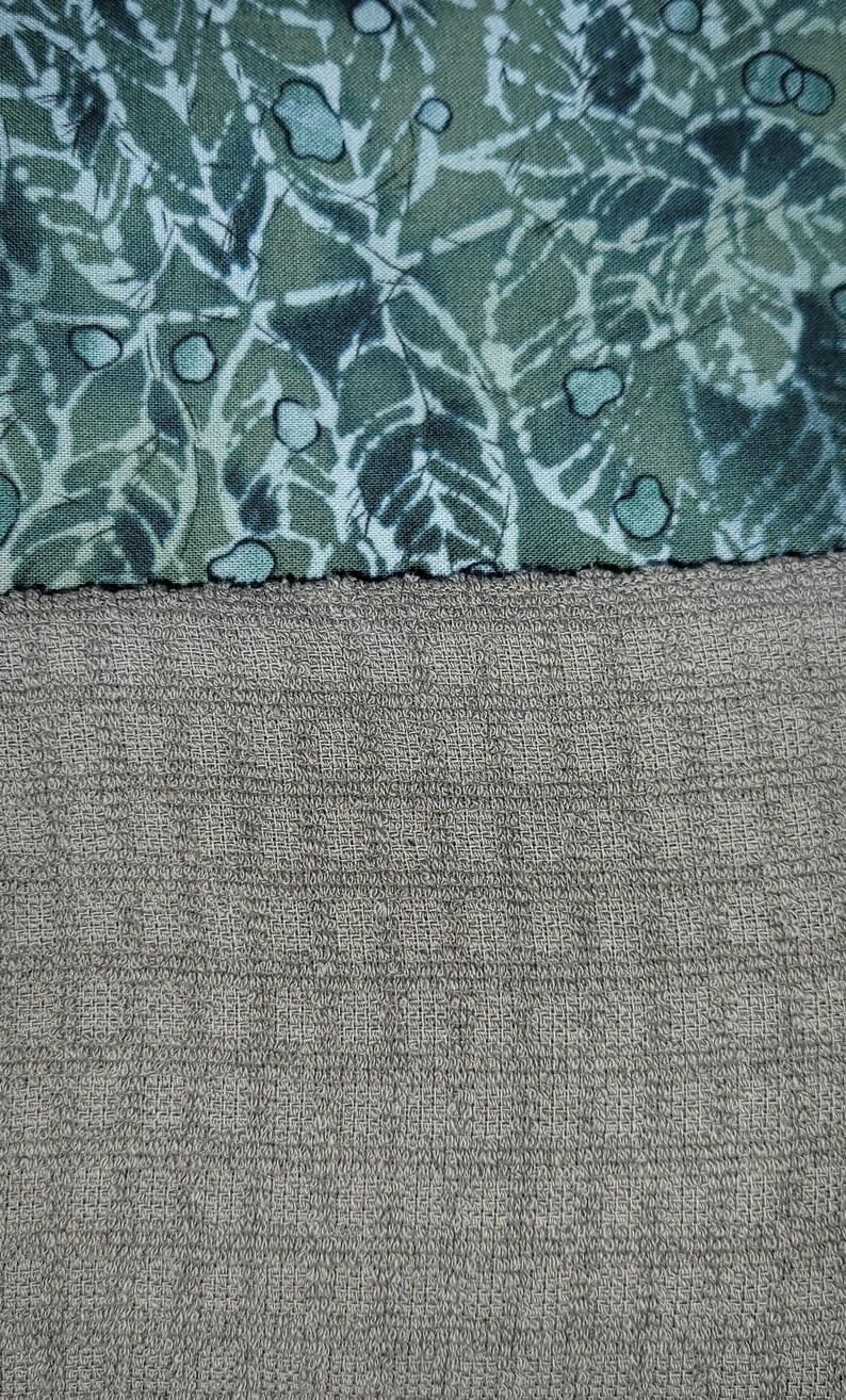 May include: A close-up of two different fabrics. The top fabric is a green and white patterned fabric. The bottom fabric is a grey textured fabric.